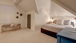 A bedroom with a sloped ceiling, a bed, a bench, and a small table.