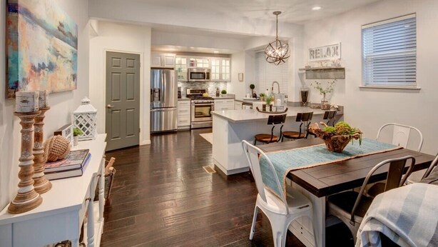 A modern kitchen with stainless steel appliances, a dining area with a wooden table, and a living space with a large painting.