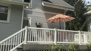 A house with a white railing, a red umbrella, and a green tree in the background.