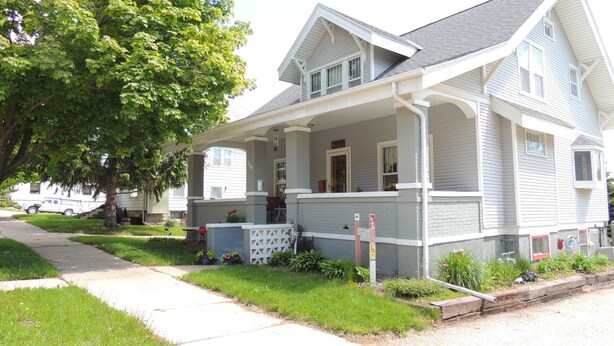A two-story house with a porch, a driveway, and a tree.