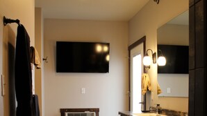 A modern bathroom with a dark wood vanity, a large mirror, and a flat-screen TV mounted on the wall. - Penthouse in the heart of Downtown Fargo with private rooftop patio (Fargo)