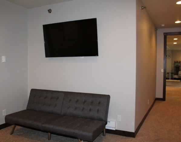 A room with a dark brown sofa, a flat-screen TV mounted on the wall, and a carpeted floor.