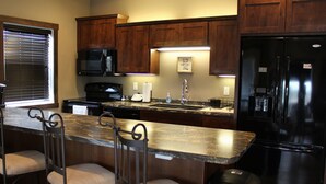 A kitchen with wooden cabinets, a black refrigerator, a microwave, a sink, and a bar stool. - Penthouse in the heart of Downtown Fargo with private rooftop patio (Fargo)