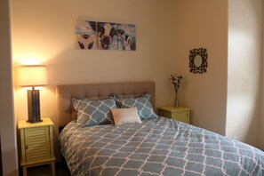 A bedroom with a bed, a nightstand with a lamp, a wall art piece, and a decorative mirror. - Penthouse in the heart of Downtown Fargo with private rooftop patio (Fargo)