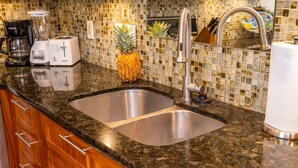 A kitchen with a double sink, wooden cabinets, a toaster, a blender, and a pineapple on the counter. - Ma'alaea Surf, Unit G9-2BR Beachfront Condo, AC, Wi-Fi, TV, Pool, Kitchen (Kihei)