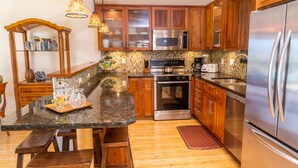 A modern kitchen with wooden cabinets, stainless steel appliances, a granite countertop, and pendant lighting. - Ma'alaea Surf, Unit G9-2BR Beachfront Condo, AC, Wi-Fi, TV, Pool, Kitchen (Kihei)
