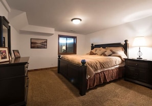 Quarto com cama, cómoda, mesa de cabeceira e uma moldura em cima da cómoda.