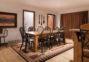 Uma área de refeições com mesa e cadeiras de madeira, tapete estampado e um quadro na parede.