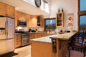 A modern kitchen with wooden cabinets, stainless steel appliances, a large island, and a view of the mountains.