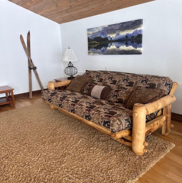 A wooden sofa with a patterned cushion, a wooden table, a lamp, and a painting of a landscape on the wall. - 6-BR Teton View Ranch with Hot Tub (Driggs)