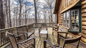A wooden deck with wicker furniture and a view of a forest. - CIDER CABIN - Brown County's Finest Log Cabin (Nashville)