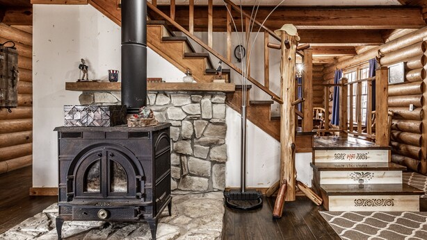 A log cabin interior with a stone fireplace, wooden staircase, and a black wood stove. - CIDER CABIN - Brown County's Finest Log Cabin (Nashville)