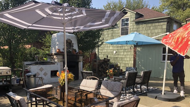 Une terrasse extérieure avec des chaises en osier, une table à plateau en verre et des parasols à rayures.