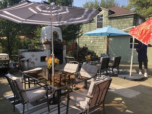 An outdoor patio with wicker chairs, a glass-top table, and striped umbrellas.