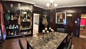 A dining area with a marble table, black chairs, a chandelier, and a display cabinet with various items.