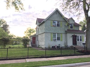 A two-story house with a gabled roof, green shutters, and a red door.