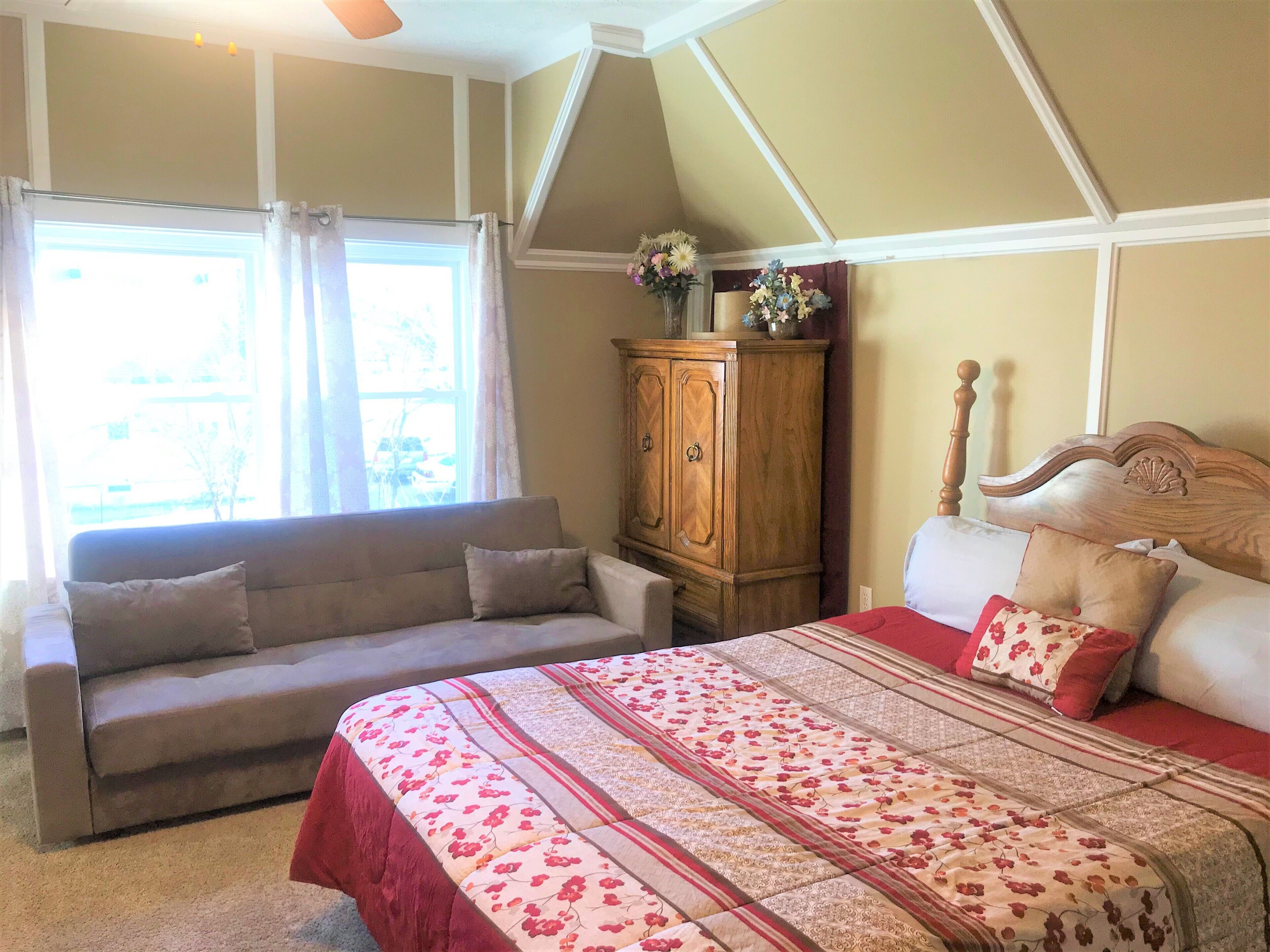 Een slaapkamer met een bed, een slaapbank, een houten kast en een raam met gordijnen.