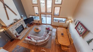A spacious living room with a stone fireplace, a large sectional sofa, a wooden dining table, and a large window offering a view of the outdoors. - Dog Friendly Deep Creek Escape w/ Mountain Views (McHenry)