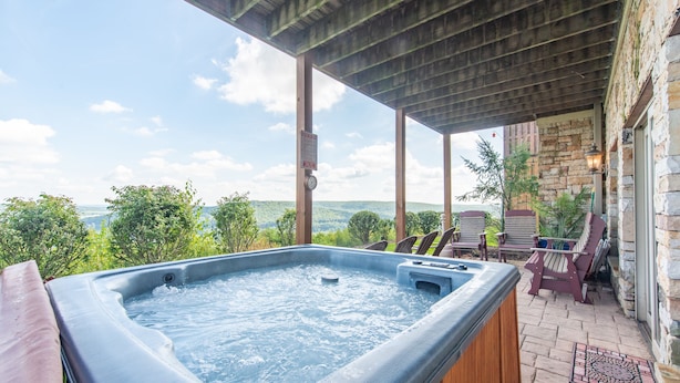 A hot tub with a wooden deck and stone walls, overlooking a scenic landscape. - Dog Friendly Deep Creek Escape w/ Mountain Views (McHenry)