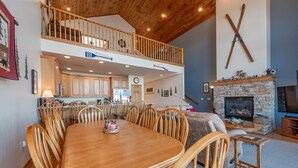 A spacious dining area with a wooden table and chairs, a kitchen with wooden cabinets, a fireplace, and a balcony with wooden railings. - Dog Friendly Deep Creek Escape w/ Mountain Views (McHenry)
