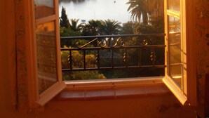 Een kamer met een groot raam, uitzicht op een waterpartij, een balkon en een stadsgezicht.