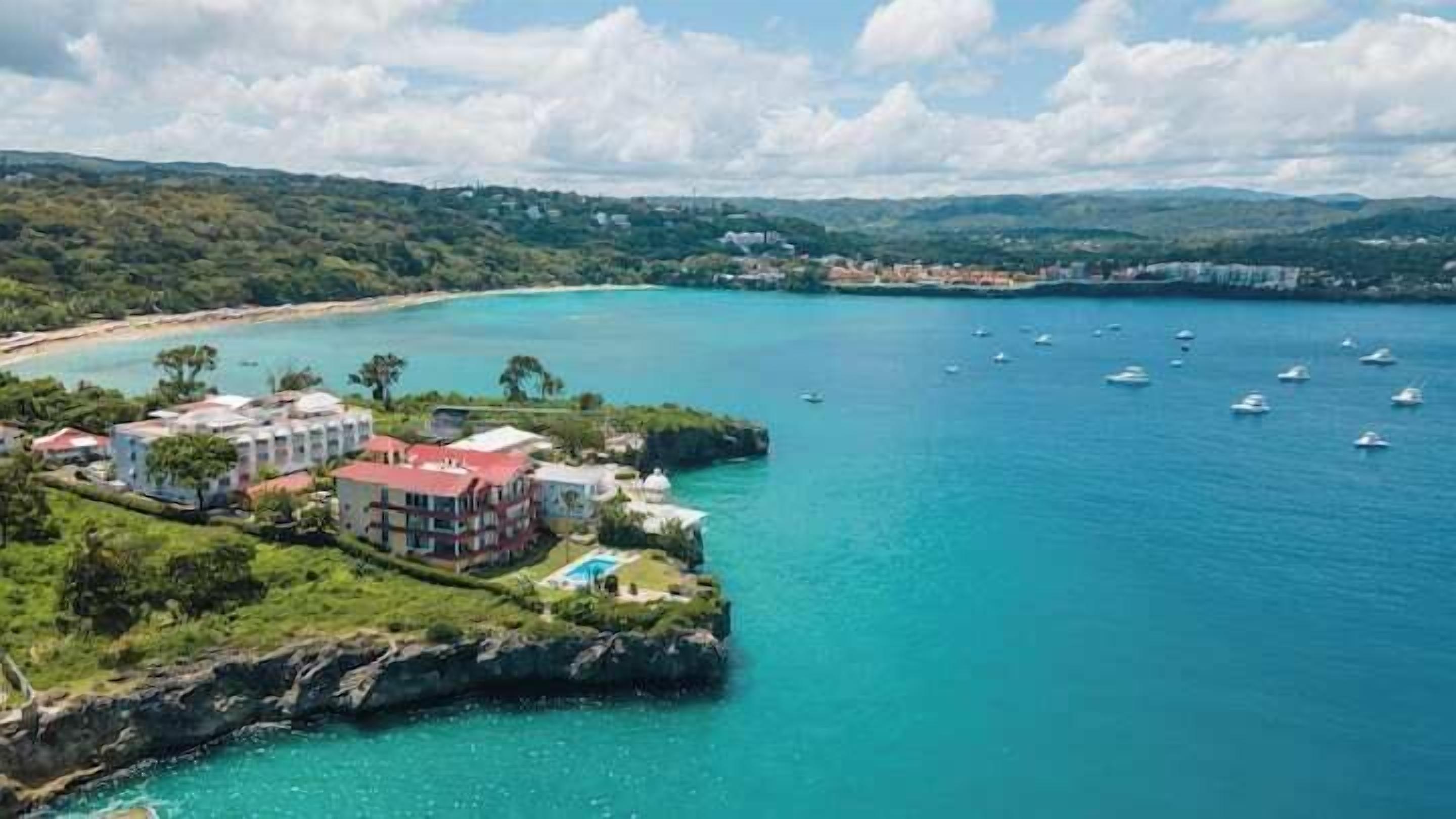 A coastal hotel with multiple buildings, a beach, and boats in the water.