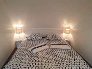 Ein ordentlich bezogenes Bett mit gemustertem Bettbezug und Kissen, begleitet von zwei Nachttischlampen auf passenden Nachttischen.