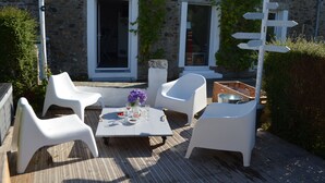 A stone building with a wooden deck, white plastic chairs, a table with a vase of flowers, and a directional sign. - In a "fisherman's house" spirit, between Finistère and the pink granite coast (Plouezoc'h)