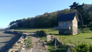 A stone house with a sloped roof, a small porch, and a view of a grassy field and trees. - In a "fisherman's house" spirit, between Finistère and the pink granite coast (Plouezoc'h)