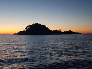 Eine Küstenlandschaft mit einer kleinen Insel, die vor einem Sonnenuntergang in Silhouette steht.