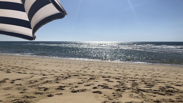 A beach with footprints in the sand and a striped umbrella. - House in Moliets et Maâ for 5 people (Moliets-Et-Maa)