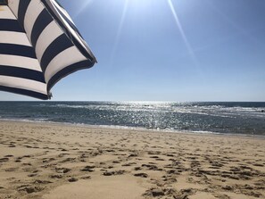 A beach with footprints in the sand and a striped umbrella.
