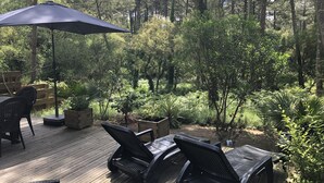 A deck with outdoor furniture and a large umbrella, surrounded by dense greenery and trees. - House in Moliets et Maâ for 5 people (Moliets-Et-Maa)