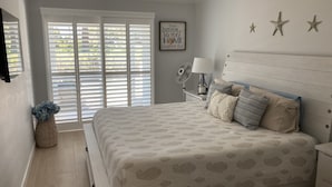 Un dormitorio con cama, mesita de noche, lámpara y un adorno en la pared.