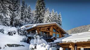 A wooden lodge with a balcony, surrounded by snow-covered trees and a clear sky. - Chalet Timan - ski-in ski-out break for 8, spa & views - OVO Network (La Clusaz)