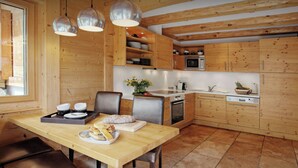 A wooden interior with a dining table, chairs, a kitchen area with appliances, and pendant lighting. - Chalet Timan - ski-in ski-out break for 8, spa & views - OVO Network (La Clusaz)