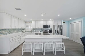 A modern kitchen with white cabinetry, a large island with bar stools, stainless steel appliances, and a tiled backsplash.