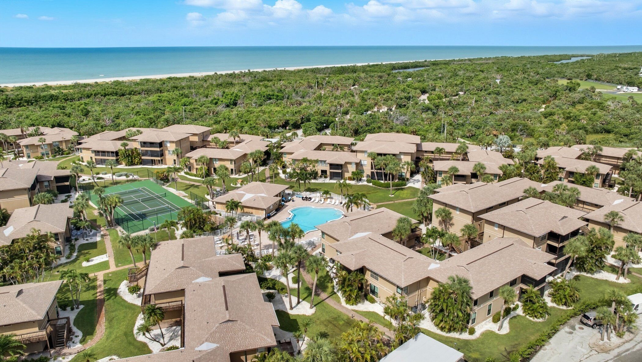 Resort com vários edifícios, piscina, quadras de tênis e vista para a praia.