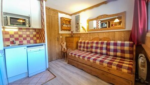 A compact room with a kitchenette, a wooden sofa, and a small wooden chair.