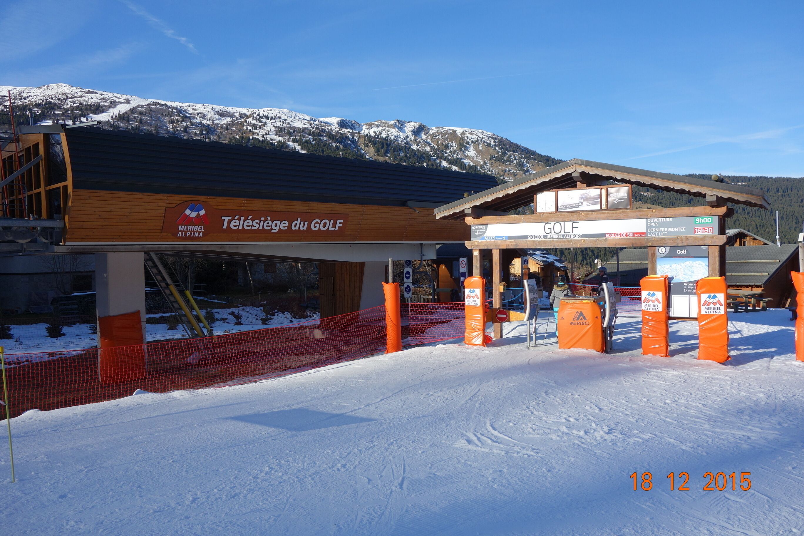 Un bâtiment d’une station de ski avec une façade en bois, un espace abrité pour le matériel et un télésiège en arrière-plan.