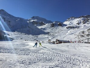 Pista nevada para esquiar con esquiadores, un telesilla y montañas al fondo.