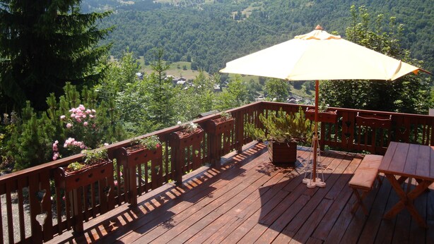 Un terrazzo in legno con tavolo e sedie, affacciato su un paesaggio montuoso.