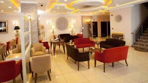 Un hall d’hôtel au design moderne, avec un mélange de fauteuils rouges et beiges, un grand piano et un escalier menant aux étages supérieurs.