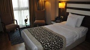 Une chambre d’hôtel comprenant un lit, deux fauteuils, une petite table agrémentée d’un objet décoratif et deux lampes murales.