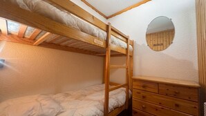 Un letto a castello con una cassettiera in legno e uno specchio rotondo appeso al muro.