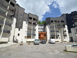 A multi-story residential building with balconies, a central entrance, and a parking area.