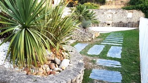 A stone pathway leading through a garden with palm plants and a stone wall in the background. - Magnificent charming villa with private pool in Sorgues 10 minutes from Avignon  (Sorgues)