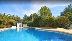 A clear blue swimming pool surrounded by lush greenery and a white building. - Villa Robert. Smart detached Villa with communal pool and fully fenced garden (Calpe)
