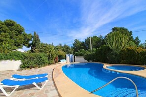 A swimming pool with blue lounge chairs, surrounded by greenery and trees.