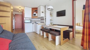 A compact living space with a kitchenette, a dining area with a table and benches, and a sofa.
